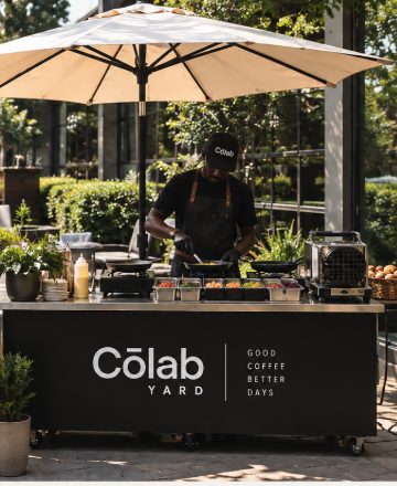 The Cōlab brunch cart in the yard under a canvas umbrella, with someone cooking at it